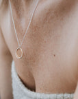 Close-up of a person wearing the Becoming Jewelry Friendship Circles Necklace, a perfect gift. The mixed metal double-ring pendant rests elegantly against bare skin, complemented by a textured light-colored top.