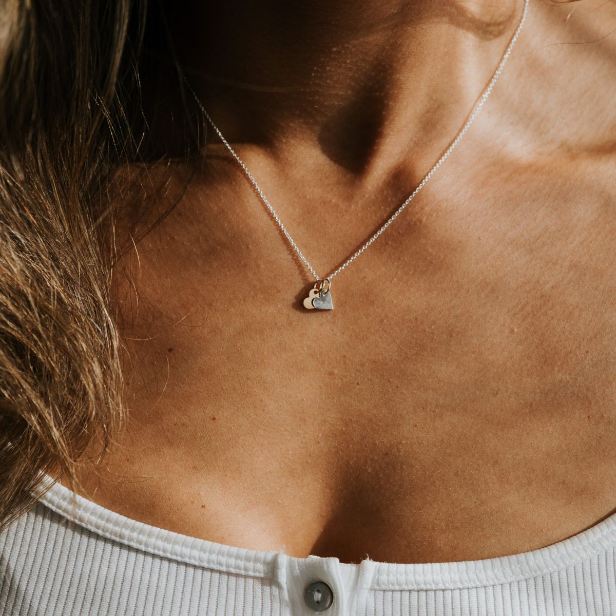 A person wearing a white button-up top and the Tiny Hearts Necklace by Becoming Jewelry, featuring mixed metal hearts, seen from the neck down—an ideal friendship necklace or perfect gift for someone special.