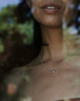 Close-up of a woman's neck and lower face, adorned with Becoming Jewelry's Friends Beads Necklace—a delicate silver accessory featuring a pendant shaped like two intricately intertwined circles, symbolizing the deep bond between dearest friends—set against a blurry, leafy background.