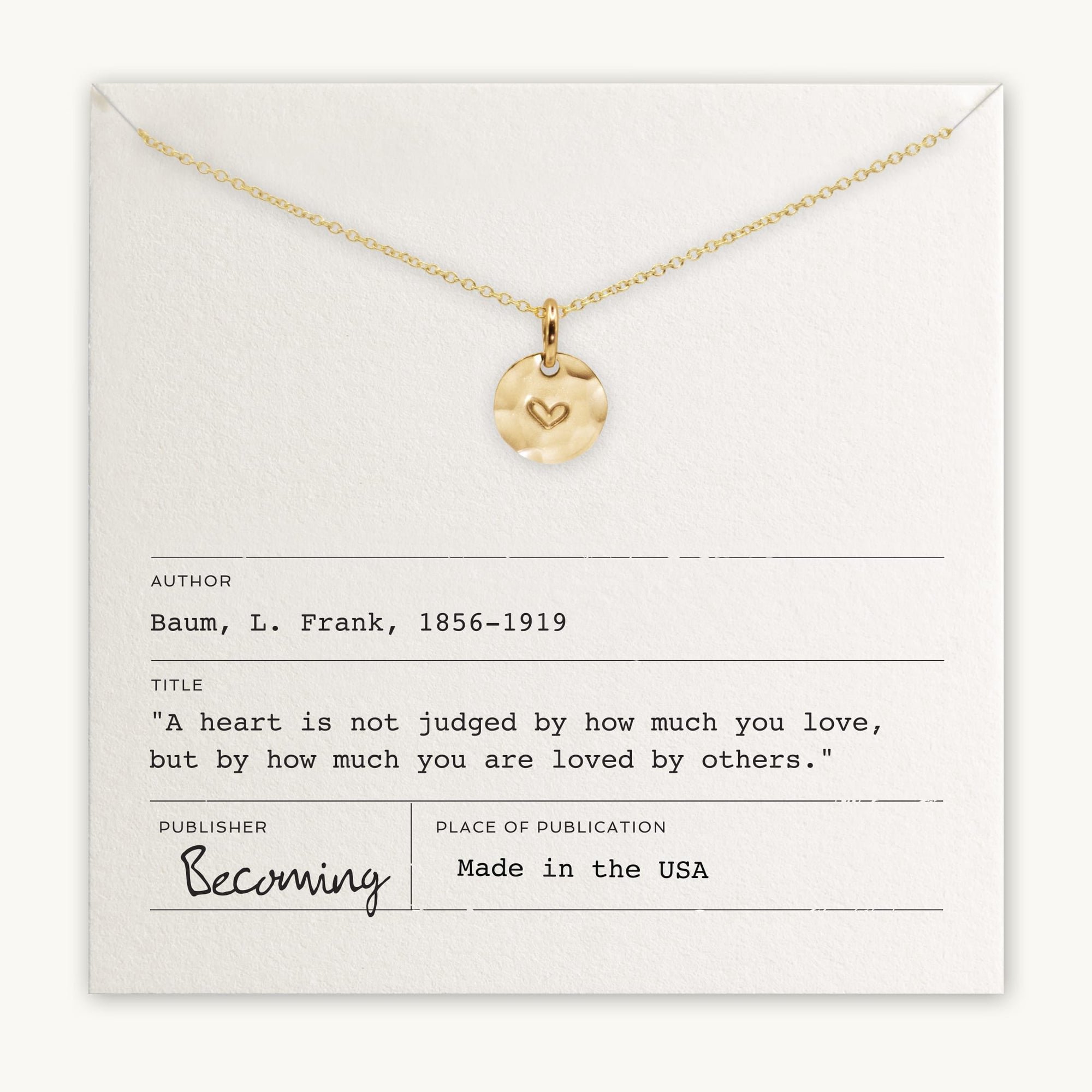 Becoming Jewelry's Heart Necklace, featuring a small heart pendant, is elegantly displayed on a card with an inspiring quote from L. Frank Baum: "A heart is not judged by how much you love, but by how much you are loved by others." Made in the USA, this beautiful piece makes for a deeply meaningful gift.