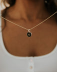 A person wears the Becoming Jewelry Heart Necklace, with its gold round pendant featuring a tiny heart engraving, against a white button-up top—an exquisite gift cherished by others.