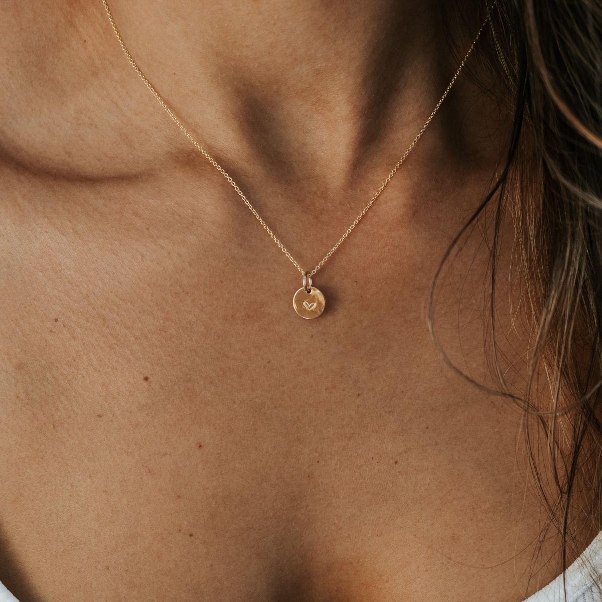 A woman wearing the Becoming Jewelry Heart Necklace with a gold heart-engraved pendant, perfect as a meaningful gift that is loved by others.