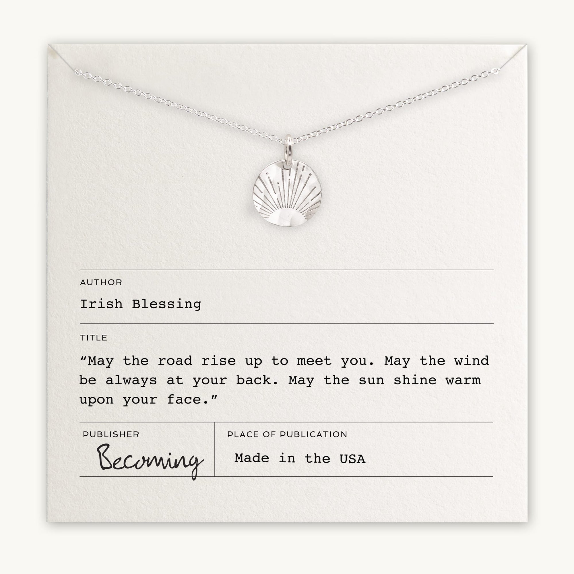 The Irish Blessing Necklace by Becoming Jewelry is showcased on a card adorned with an Irish blessing. The card reads: "May the road rise up to meet you. May the wind be always at your back. May the sun shine warm upon your face." This silver necklace, featuring a sun pendant, makes a perfect gift, wishing luck on any new adventure.