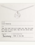 The Irish Blessing Necklace by Becoming Jewelry is showcased on a card adorned with an Irish blessing. The card reads: "May the road rise up to meet you. May the wind be always at your back. May the sun shine warm upon your face." This silver necklace, featuring a sun pendant, makes a perfect gift, wishing luck on any new adventure.