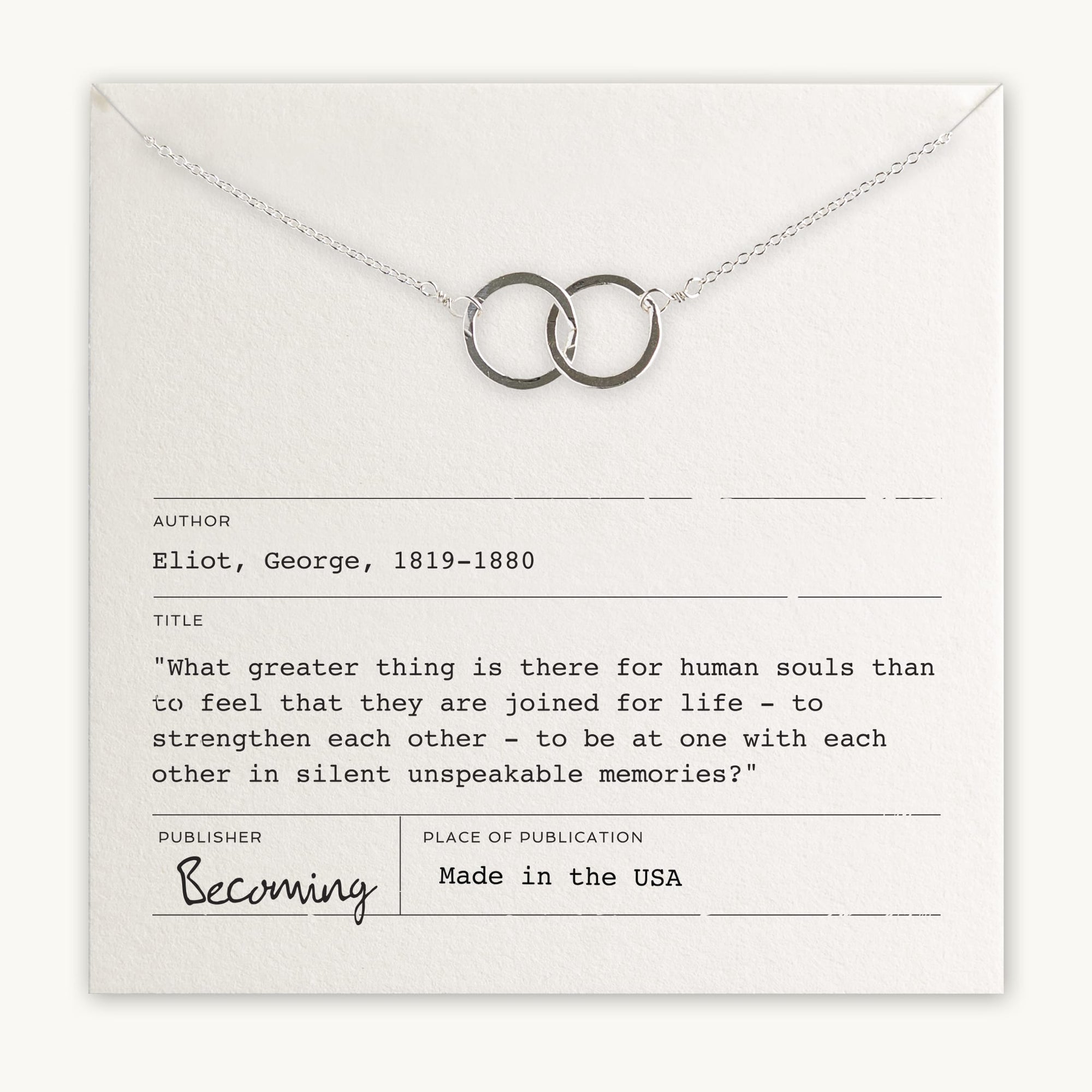 A Joined for Life necklace with intertwined circles lies on a card quoting George Eliot (1819-1880) about human connection. The card indicates the quote is from Becoming Jewelry and notes it was made in the USA.