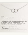 A Joined for Life necklace with intertwined circles lies on a card quoting George Eliot (1819-1880) about human connection. The card indicates the quote is from Becoming Jewelry and notes it was made in the USA.