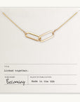 The Linked Together Necklace from Becoming Jewelry showcases a gold chain with two interwoven links and is beautifully presented on a card that reads "Linked together." Made in the USA, this exquisite piece symbolizes connection and unity, making it an ideal gift.