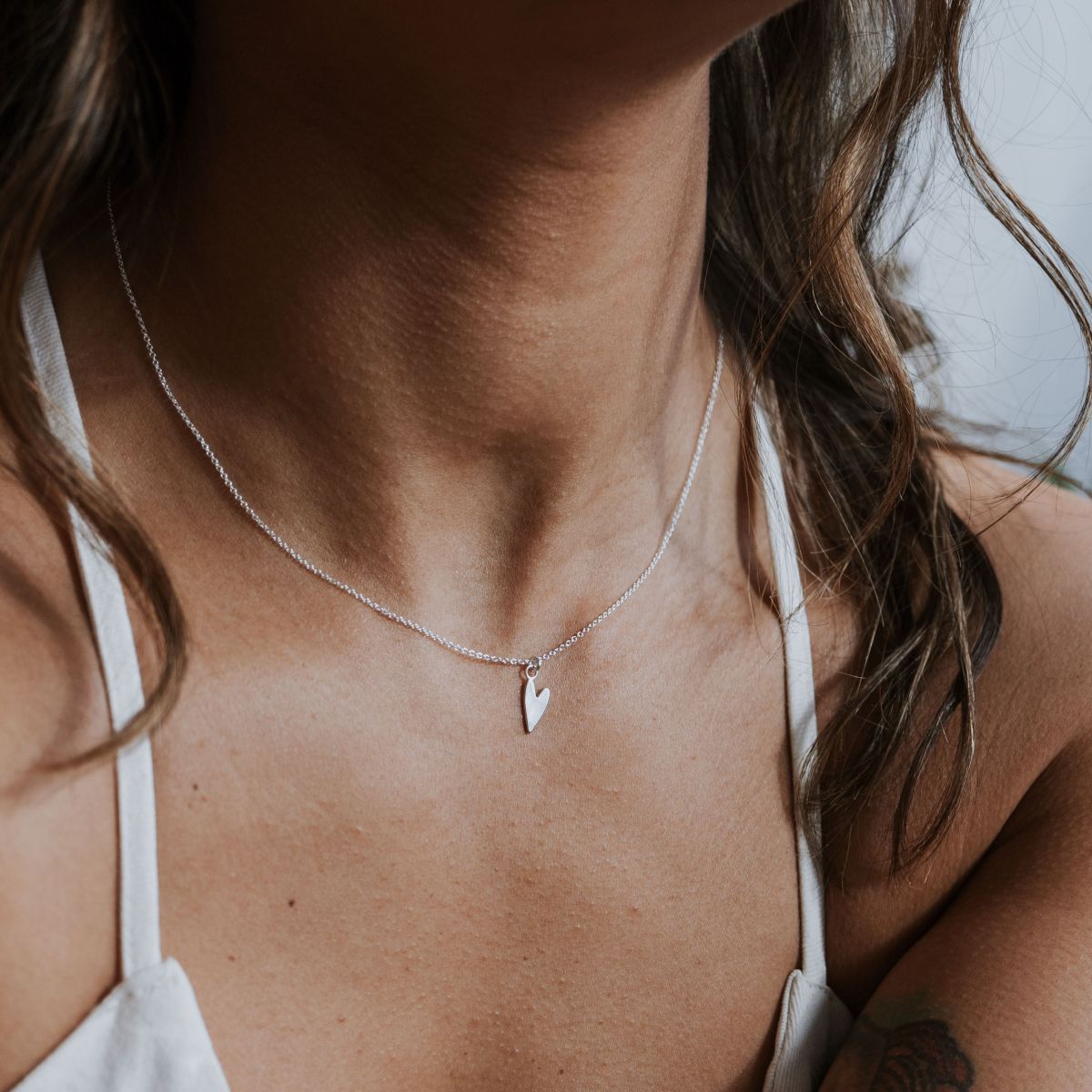 A person wears Becoming Jewelrys Love Deeply Necklace, featuring a delicate heart charm in silver, visible from the neck down and exuding subtle elegance.