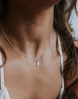 A person wears Becoming Jewelrys Love Deeply Necklace, featuring a delicate heart charm in silver, visible from the neck down and exuding subtle elegance.
