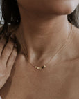 A close-up of the Becoming Jewelry Mothers & Daughters Necklace reveals its elegant gold design with small circular pendants, captured against a softly blurred background. Resting by her neck, it symbolizes the timeless bond between strong mothers and daughters.