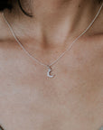 Close-up of a person wearing a thin silver chain necklace with a crescent moon pendant—an elegant and meaningful piece known as the Love You To The Moon Necklace by Becoming Jewelry. The person is dressed in a light-colored top, making the necklace stand out beautifully.