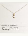 The Love You To The Moon Necklace by Becoming Jewelry is a delicate gold piece featuring a crescent moon pendant and displayed on a card with the words "Love you to the moon and back." Made in the USA, this meaningful necklace serves as a daily reminder of love and affection.
