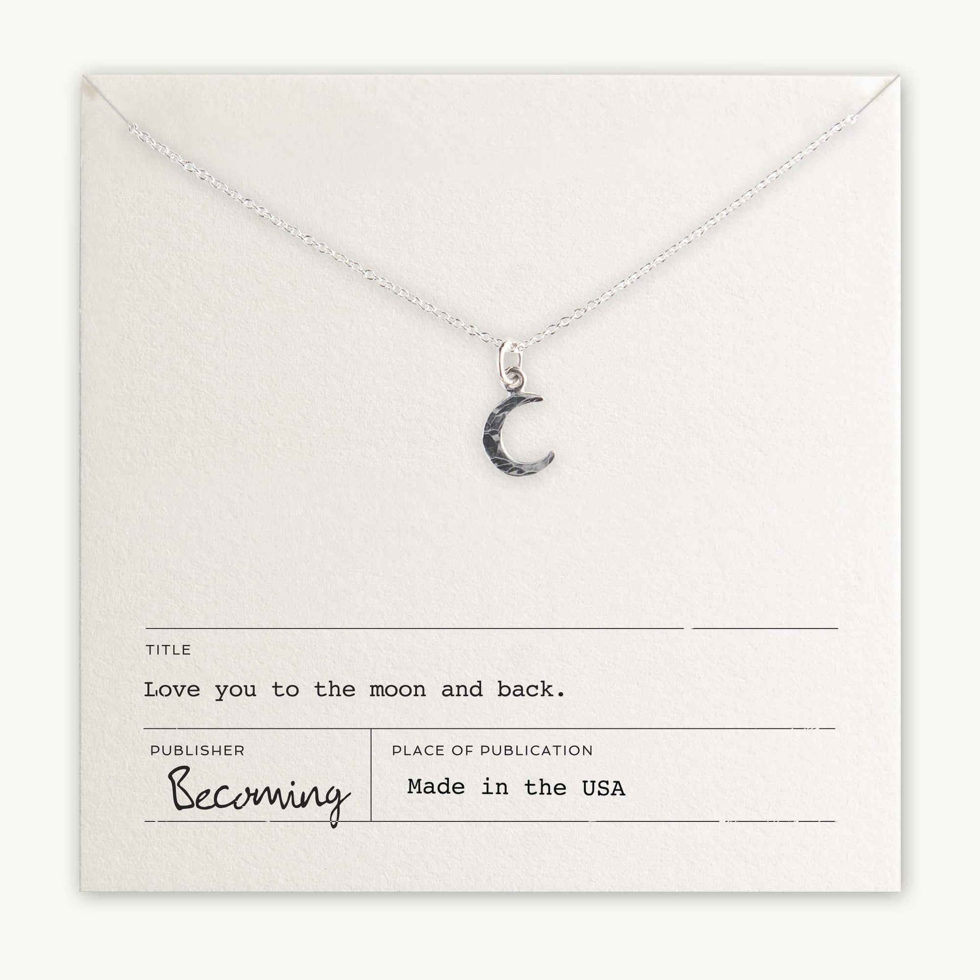 The "Love You To The Moon Necklace" by Becoming Jewelry features a silver crescent moon pendant on a card that reads, "Love you to the moon and back" and "Becoming, Made in the USA." This meaningful piece serves as a daily reminder of your affection.