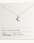 The "Love You To The Moon Necklace" by Becoming Jewelry features a silver crescent moon pendant on a card that reads, "Love you to the moon and back" and "Becoming, Made in the USA." This meaningful piece serves as a daily reminder of your affection.