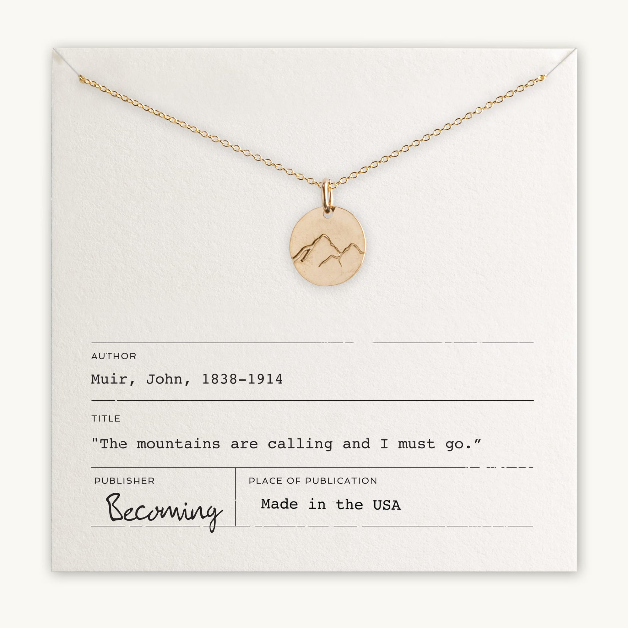 The Mountains Are Calling Necklace by Becoming Jewelry features a gold necklace with a small mountain charm pendant showcasing a mountain design. It comes on a card with the quote: "The mountains are calling and I must go" by John Muir, making it an ideal gift for adventure and nature enthusiasts. The card reads: Becoming, Made in the USA.