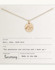 The Mountains Are Calling Necklace by Becoming Jewelry features a gold necklace with a small mountain charm pendant showcasing a mountain design. It comes on a card with the quote: "The mountains are calling and I must go" by John Muir, making it an ideal gift for adventure and nature enthusiasts. The card reads: Becoming, Made in the USA.