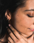 A person with long, dark hair wearing Becoming Jewelry's large Open Hoop Earrings and a beige top, gently touching their neck with their hand.