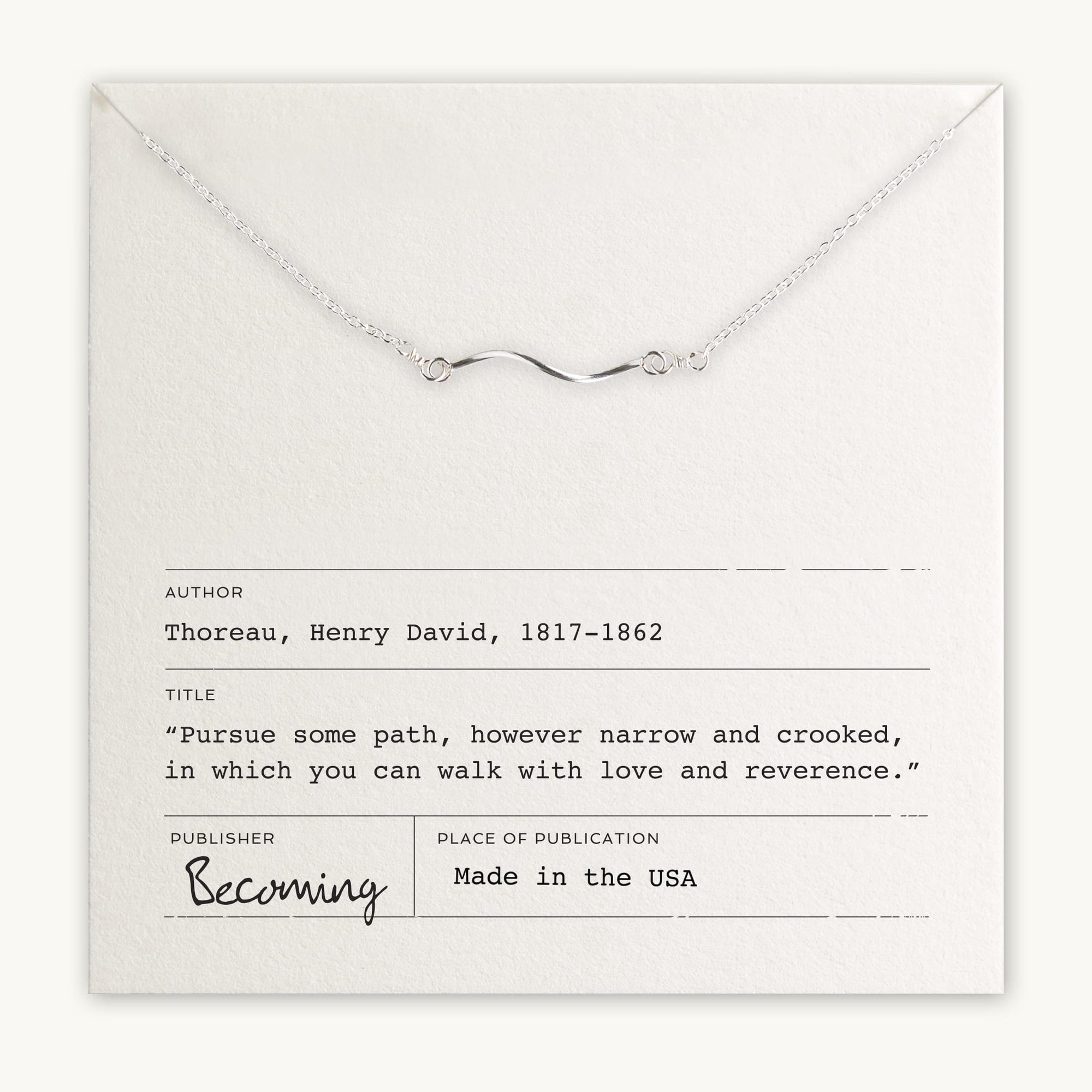 The Path Necklace, a beautiful silver accessory by Becoming Jewelry, features a wavy pendant and is displayed on a card with an inspiring quote by Henry David Thoreau. Made in the USA and published by Becoming, it offers a gentle reminder to follow one's heart, making it a meaningful gift.