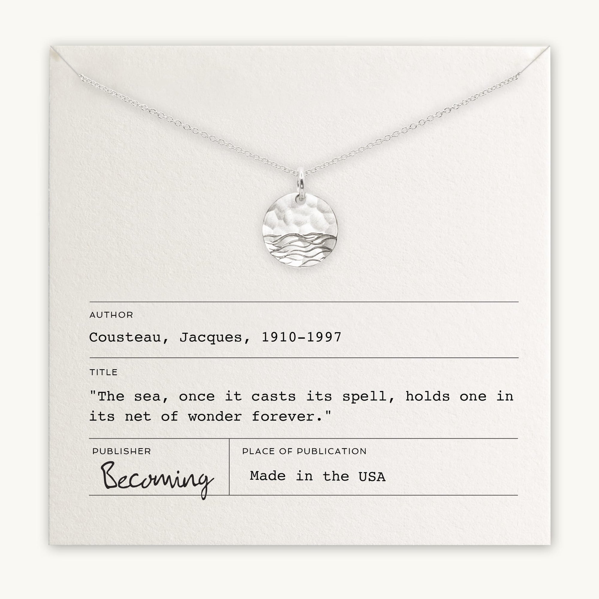 The Sea Necklace, a silver piece by Becoming Jewelry, showcases a circular pendant adorned with an ocean wave design. Presented on a card featuring a quote from Jacques Cousteau and proudly stating 'Made in the USA,' this elegant necklace is an ideal sea-inspired gift.