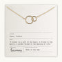 The Sisters Necklace by Becoming Jewelry features two intertwined gold circles on a delicate chain, presented on a card with an Isadora James quote about sisters. Made in the USA, this heartfelt gift beautifully symbolizes the bond between sisters.