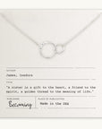 The Sisters Necklace by Becoming Jewelry is a stunning silver necklace featuring intertwined circles, elegantly placed on a card that reads, "A sister is a gift to the heart, a friend to the spirit, a golden thread to the meaning of life.