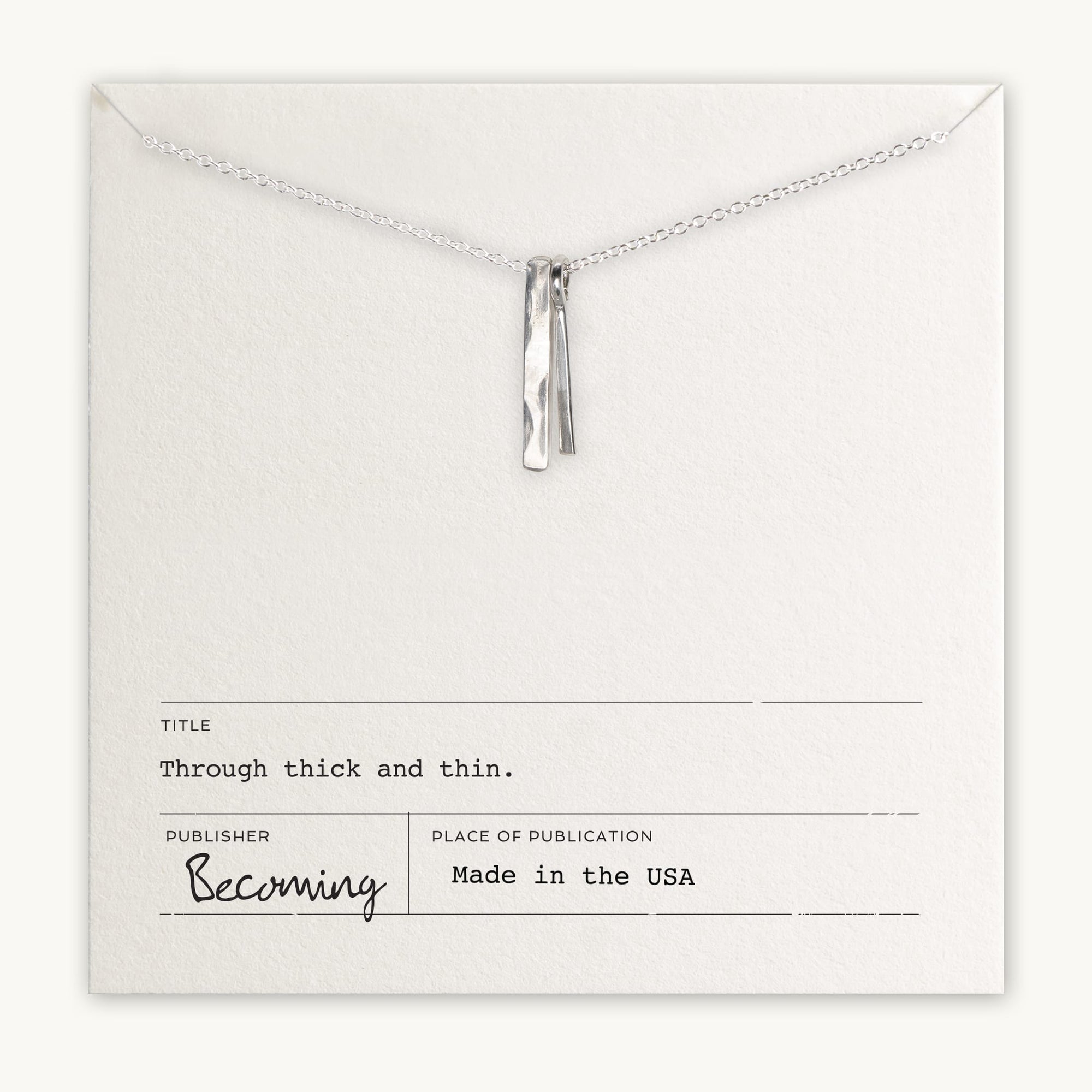 A silver necklace, a best-selling gift from Becoming Jewelry, is displayed on a card reading: Title: Through Thick & Thin. Publisher: Becoming Jewelry. Made in the USA.