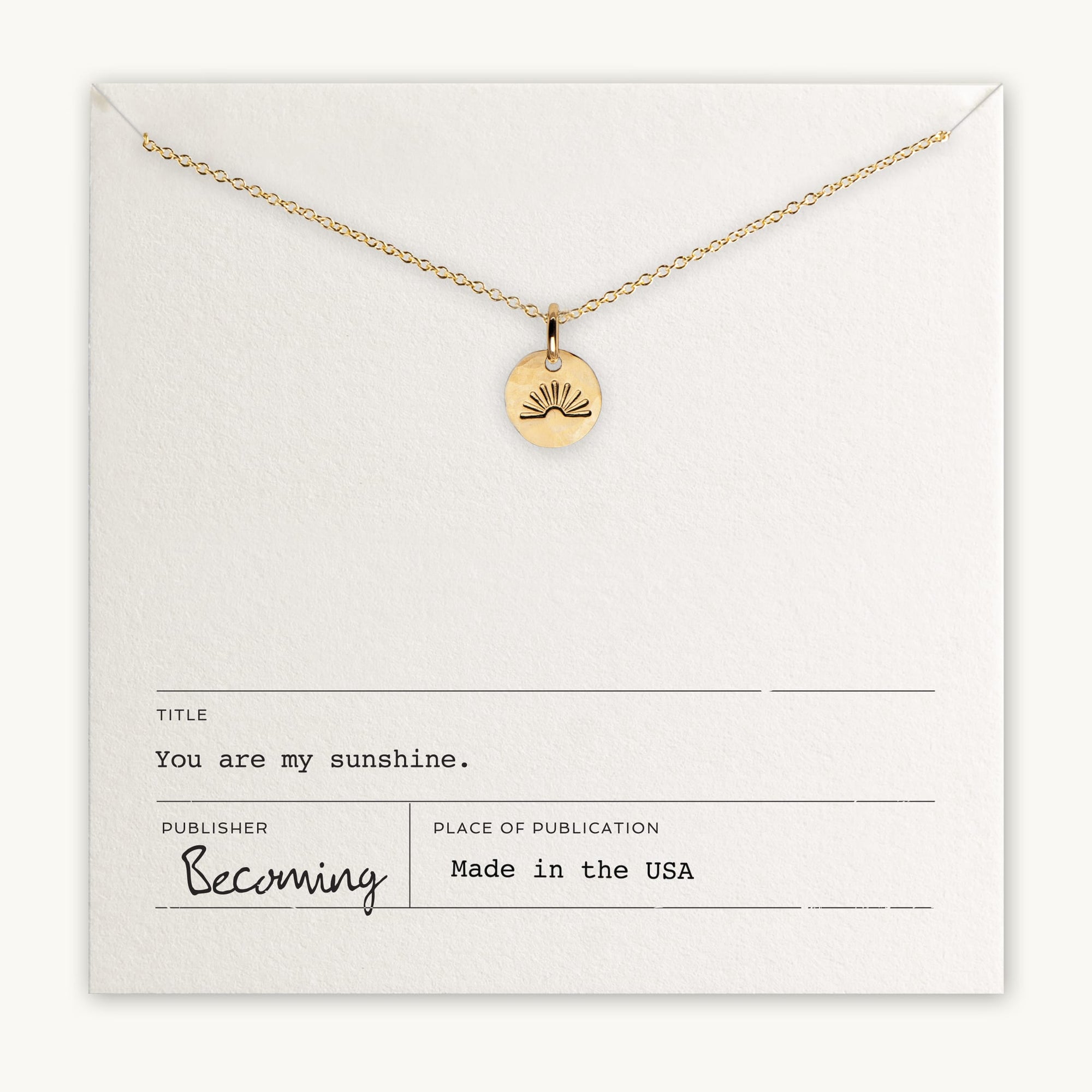 The "You Are My Sunshine Necklace" by Becoming Jewelry is a gold necklace with a round pendant featuring a radiant sun design. It is displayed on a card with the text "You are my sunshine," and it is proudly made in the USA. This bestselling necklace makes the perfect gift for someone special.
