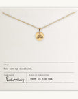 The "You Are My Sunshine Necklace" by Becoming Jewelry is a gold necklace with a round pendant featuring a radiant sun design. It is displayed on a card with the text "You are my sunshine," and it is proudly made in the USA. This bestselling necklace makes the perfect gift for someone special.