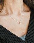 A woman wears a delicate Becoming Jewelry Blessings Necklace with a small pendant, the focus is on her neckline and the jewelry.