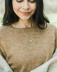 Woman wearing a brown sweater and a Family Tree Necklace by Becoming Jewelry, looking down with a gentle smile.
