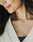 Close-up of a smiling woman wearing a delicate Becoming Jewelry gold-filled, curved Path Necklace and a cream-colored cardigan.