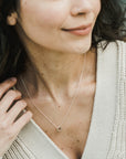 Woman wearing a delicate Becoming Jewelry Together Forever Necklace and a beige cardigan, smiling slightly off-camera.