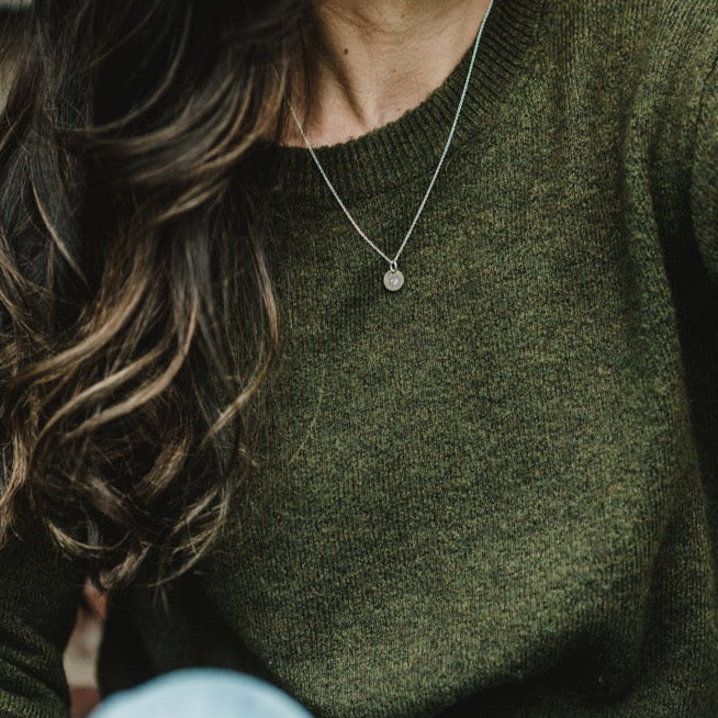 A person with long brown hair wearing a green sweater and a silver Heart Necklace by Becoming Jewelry, featuring a small heart-shaped pendant.