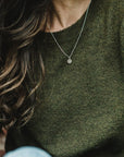 Woman wearing a green sweater and a simple gold filled Becoming Jewelry heart necklace.