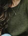 A person with long brown hair wearing a green sweater and a silver Heart Necklace by Becoming Jewelry, featuring a small heart-shaped pendant.