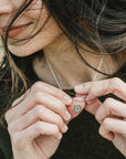 A person holding a Becoming Jewelry gold-filled horseshoe necklace on a chain, with a focus on the hands and the pendant.