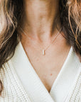 Woman wearing a Becoming Jewelry Pillar of Strength Necklace with a hammered bar drop charm paired with a white knitted top.