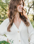 Woman smiling outdoors in a white cardigan, wearing a Becoming Jewelry sterling silver Pillar of Strength Necklace with a hammered bar drop charm.