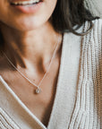 A close-up of a person wearing a light-colored knitted sweater and the Light Within Necklace by Becoming Jewelry, which features a round pendant adorned with a tiny starburst. The person's face is partially visible, blending seamlessly with the light within the delicate design.
