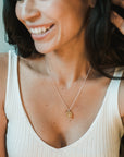 A woman wearing a white sleeveless top smiles, showcasing the North Star Necklace by Becoming Jewelry—an exquisite piece perfect as a graduation gift.
