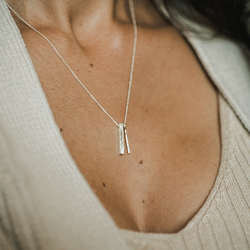 A close-up of a person&#39;s neck area showing a simple silver Through Thick &amp; Thin Necklace pendant necklace with fine cable chain on a light-colored top by Becoming Jewelry.