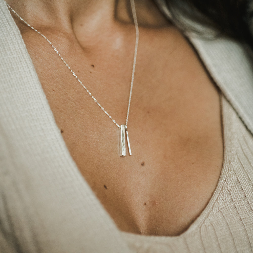 A close-up of a woman wearing a beige textured top paired with Becoming Jewelry's "Through Thick & Thin Necklace," a delicate silver piece featuring two vertical pendants and one of our best-sellers.