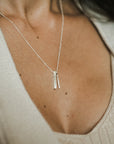 A close-up of a woman wearing a beige textured top paired with Becoming Jewelry's "Through Thick & Thin Necklace," a delicate silver piece featuring two vertical pendants and one of our best-sellers.