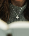 A person wearing a gray sweater and a Trees Necklace with a trees charm pendant from Becoming Jewelry.
