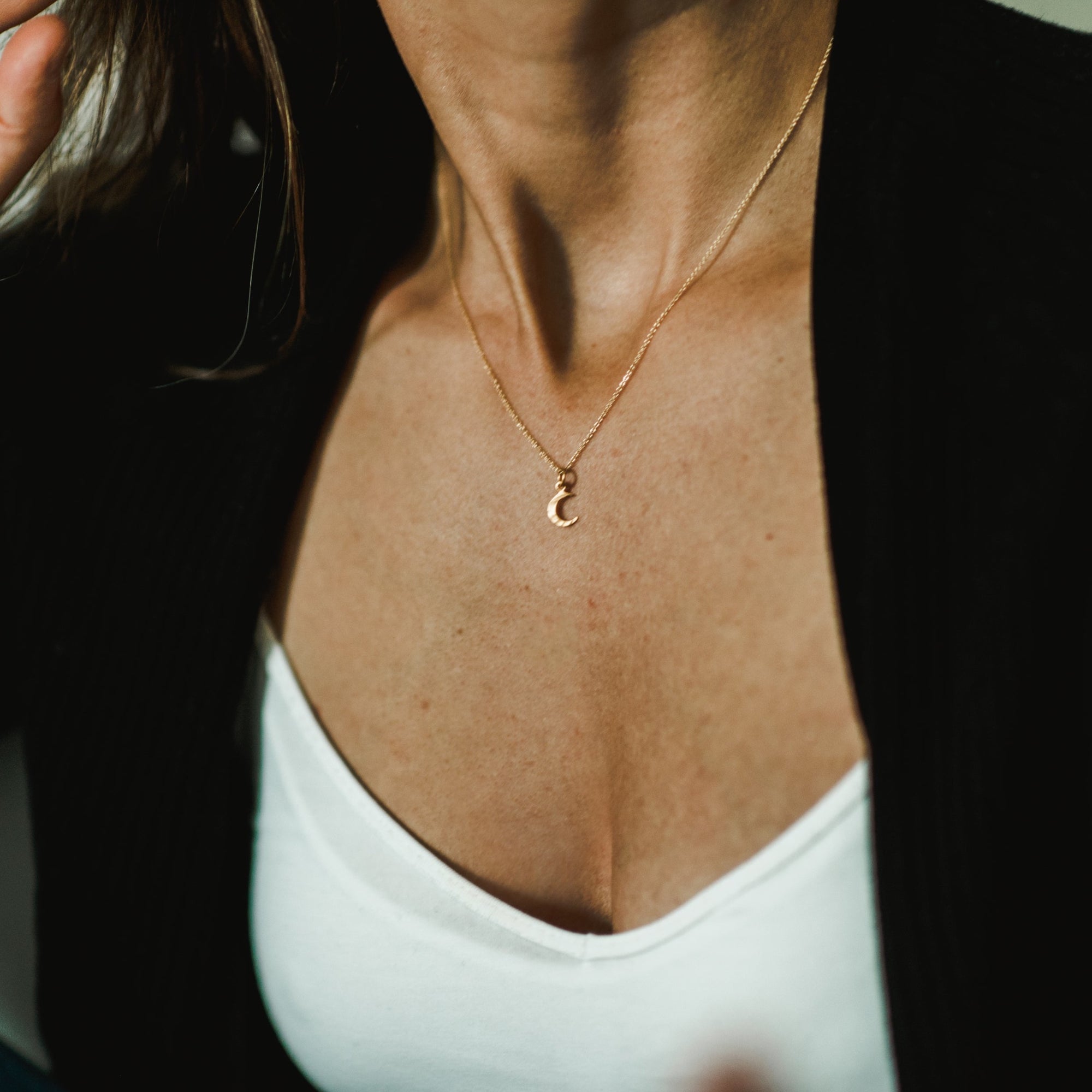 A person wearing the Becoming Jewelry Love You To The Moon Necklace with a crescent moon pendant, a white top, and a black cardigan; it's a meaningful piece that serves as a daily reminder of love.