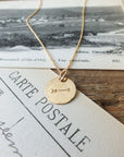 The Arrow Necklace by Becoming Jewelry, a gold pendant necklace with an arrow charm, rests on vintage black-and-white postcards, symbolizing motivation and encouragement.
