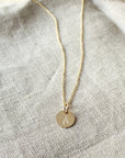 A "On Fire Necklace" pendant necklace with a heart-shaped cutout on a linen background by Becoming Jewelry.