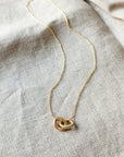 A Linked By Blood Necklace by Becoming Jewelry with a knot pendant lying on a fabric surface.