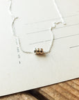 A delicate Three Things Necklace by Becoming Jewelry with three small beads displayed on a piece of paper with lines.