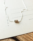 The delicate Three Things Necklace by Becoming Jewelry features a silver chain adorned with three small gold beads, embodying grace. It is displayed on beige paper with faint lines and text, placed on a wooden surface.